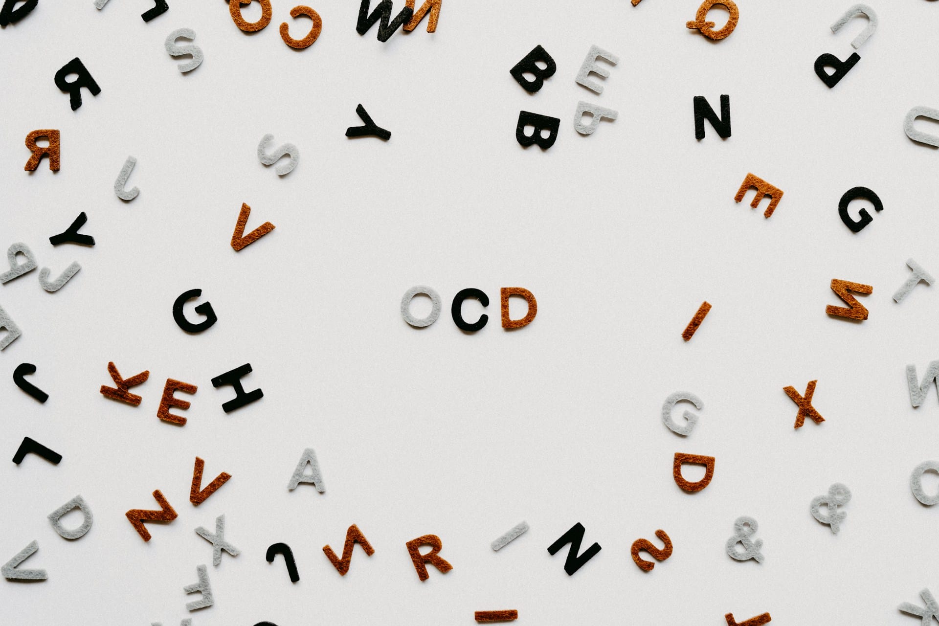 Scattered black, white, and brown alphabet letters surround the word “OCD” spelt out in the centre on a white background, hinting at the support that approaches like DBT can offer.